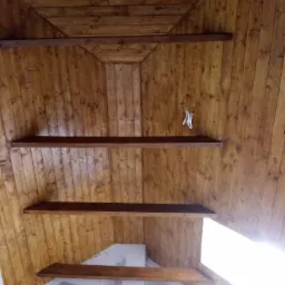 Drewniany sufit poddasza z widocznymi belkami konstrukcyjnymi, oświetlony naturalnym światłem wpadającym przez okno dachowe, z wiszącym w rogu wieszakiem na ubrania.