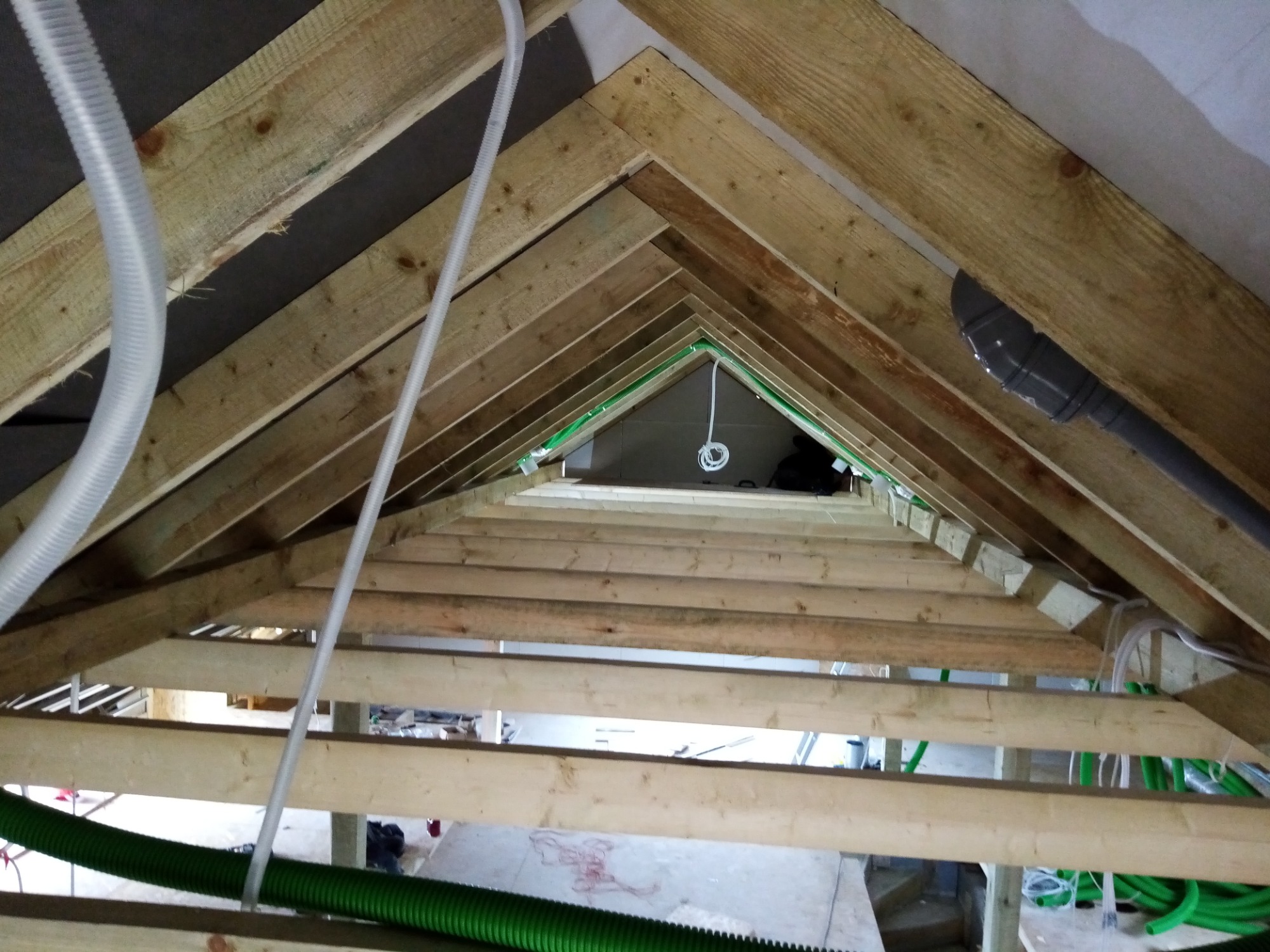 Drewniana konstrukcja dachu poddasza z widocznymi przewodami wentylacyjnymi i instalacją elektryczną w trakcie montażu.