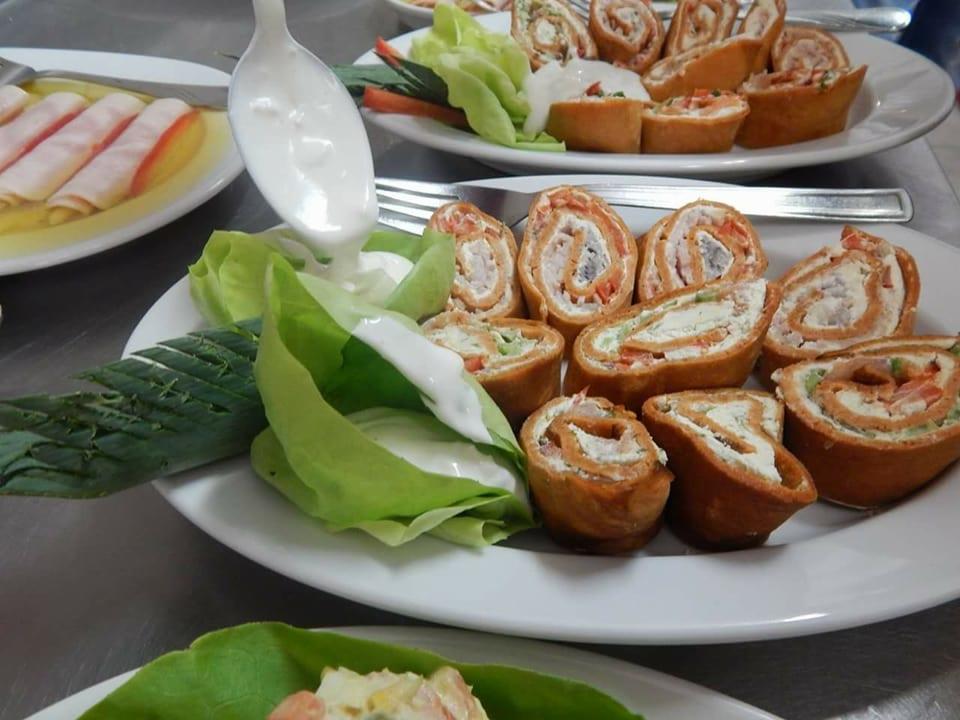 Apetycznie wyglądające roladki z nadzieniem, ułożone na talerzu z liśćmi sałaty, polane sosem, w tle talerz z szynką w galarecie i roladkami.