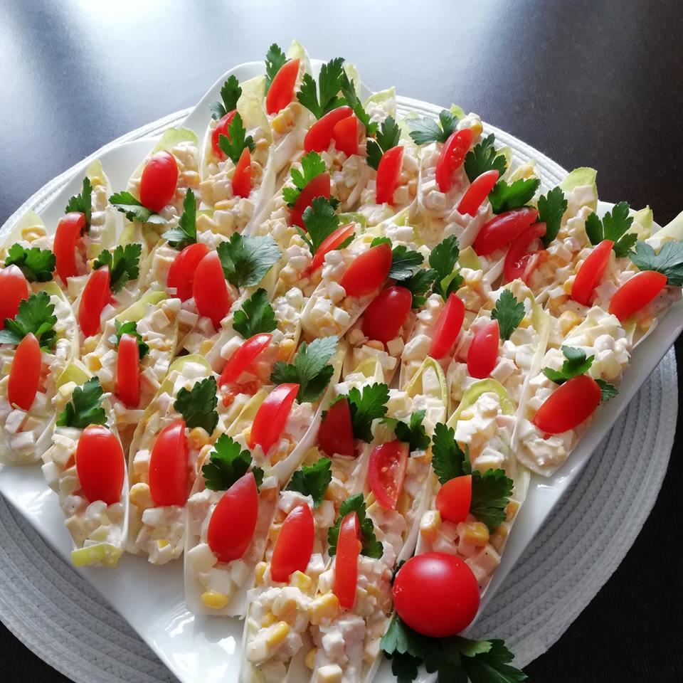 Elegancko ułożone łódeczki z cykorii wypełnione sałatką z kukurydzą, jajkiem i majonezem, udekorowane połówkami pomidorków cherry i świeżą natką pietruszki na białym talerzu.