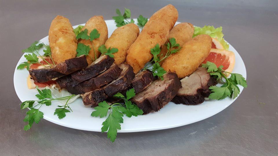 Elegancko podane danie na białym talerzu: smażone krokiety i plastry pieczonego mięsa, udekorowane świeżą natką pietruszki i cząstkami grejpfruta.