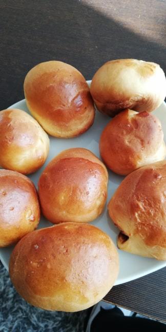 Błyszczące, złociste bułeczki drożdżowe ułożone na białym talerzu, sfotografowane w naturalnym świetle z góry.