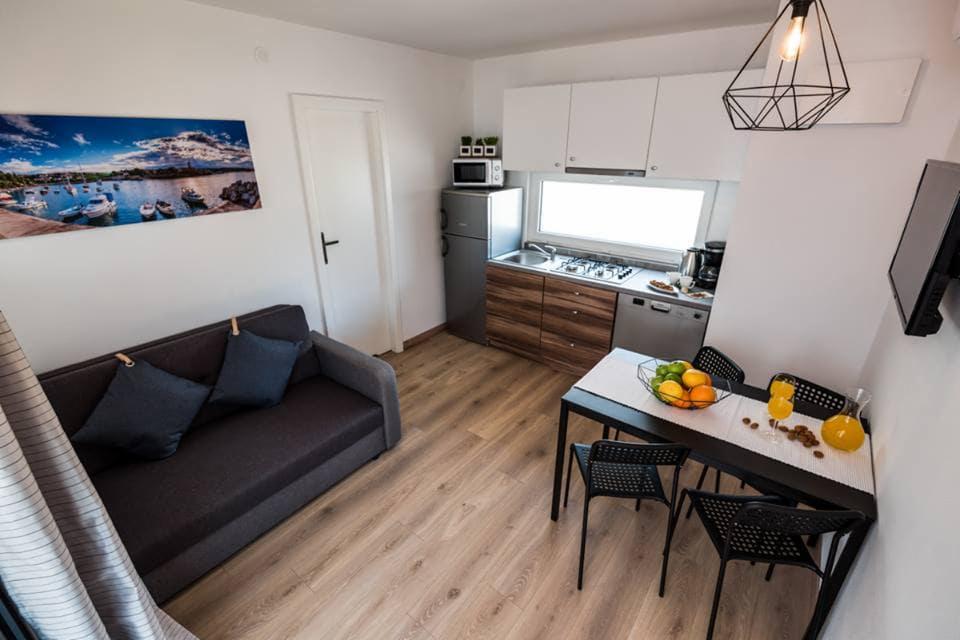 Wnętrze małego domku modułowego z aneksem kuchennym, sofą i stołem jadalnym, oświetlone wiszącą lampą w stylu industrialnym.