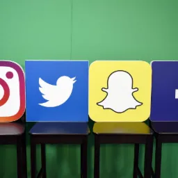 Logotypy Instagram, Twitter, Snapchat i Facebook umieszczone na czterech ciemnych krzesłach na tle zielonej ściany.