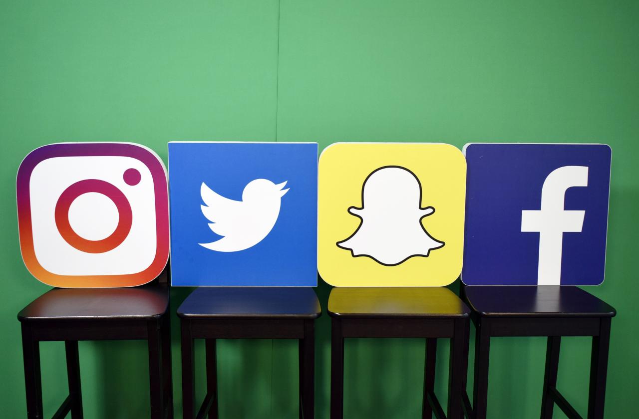 Logotypy Instagram, Twitter, Snapchat i Facebook umieszczone na czterech ciemnych krzesłach na tle zielonej ściany.