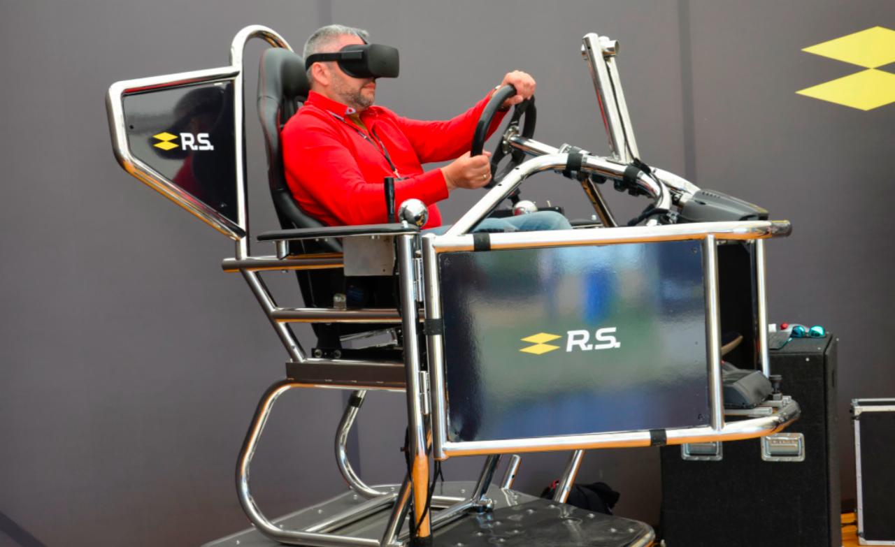 Mężczyzna w czerwonej koszuli korzysta z symulatora wyścigów z goglami VR, na metalowej konstrukcji z logo R.S.