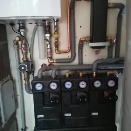 Zamontowany piec gazowy z widocznymi rurami miedzianymi i elementami instalacji grzewczej, w tym czarne moduły Afriso z manometrami.