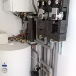 Nowoczesny układ instalacji grzewczej z białym zasobnikiem, niebieskim naczyniem wzbiorczym i czarnym rozdzielaczem z pompami obiegowymi Wilo, rury izolowane szarą pianką.