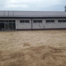 Budynek w trakcie budowy z widocznym przygotowanym terenem, lekko pochmurne niebo.