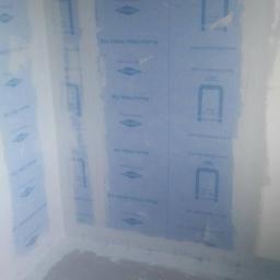 Renova Remonty i Wykończenia Wnętrz - Przygotowanie ścian w łazience do położenia płytek, zabezpieczone niebieską folią hydroizolacyjną Blanke Aqua Shield 100, widoczne łączenia zabezpieczone taśmą.