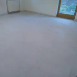 Wykończona podłoga z jasnych, kwadratowych płytek w pustym pokoju z grzejnikiem i oknem balkonowym.