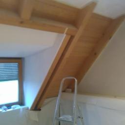 Renova Remonty i Wykończenia Wnętrz - Poddasze w trakcie adaptacji: drewniana konstrukcja dachu, okno z roletami, drabina aluminiowa, przygotowanie do malowania, widoczne taśmy malarskie.