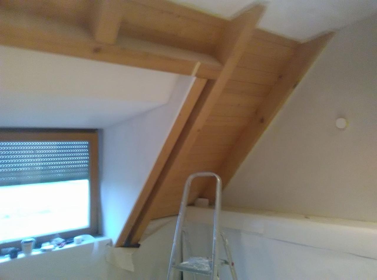 Poddasze w trakcie adaptacji: drewniana konstrukcja dachu, okno z roletami, drabina aluminiowa, przygotowanie do malowania, widoczne taśmy malarskie.