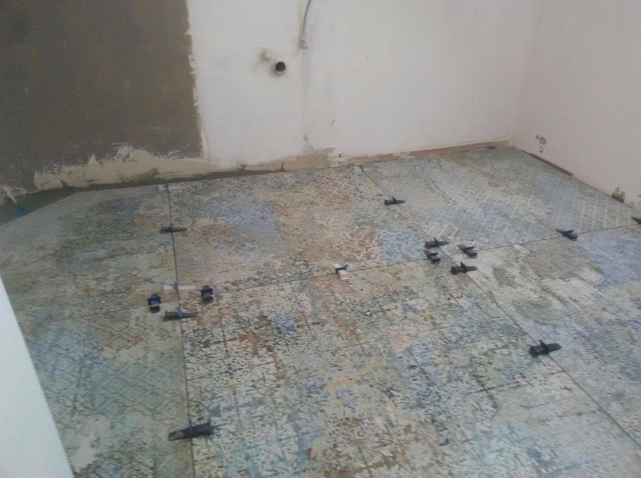 Układanie płytek podłogowych z użyciem krzyżyków poziomujących w trakcie remontu w Zawadzie. Widoczne fragmenty ścian przed malowaniem.