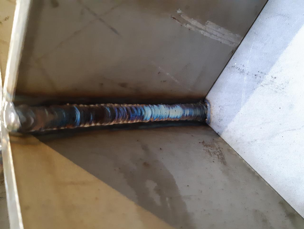 Spoina łącząca dwa elementy metalowe pod kątem prostym, widoczne przebarwienia termiczne na spoinie.