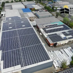 Widok z lotu ptaka na rozległą instalację fotowoltaiczną na dachach budynków przemysłowych. W tle logo firmy Solar International Construction Service.