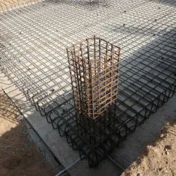 Zbrojenie fundamentu pod dom murowany, widoczne pręty pionowe i poziome tworzące siatkę zbrojeniową, przygotowane do zalania betonem.