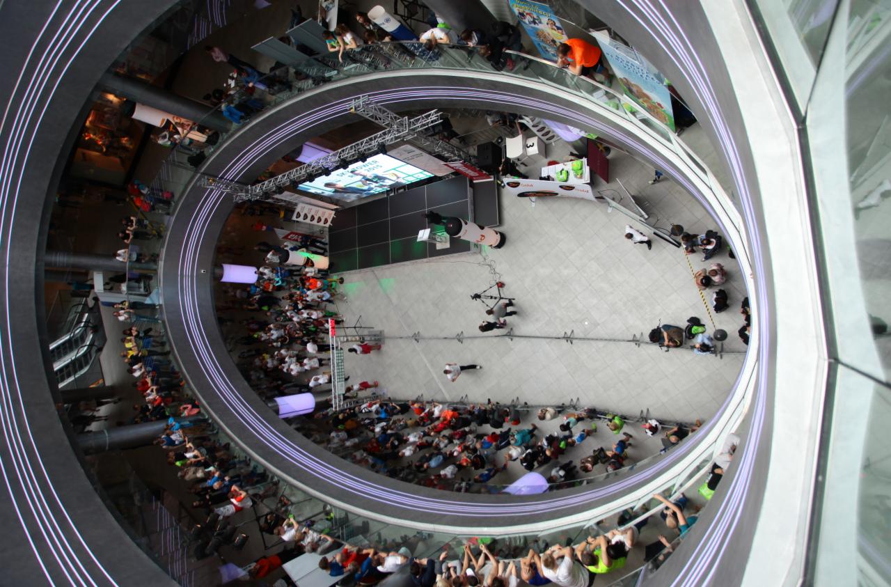 Widok z góry na scenę i widownię w atrium budynku podczas wydarzenia, z widocznymi elementami technicznymi i oświetleniem.