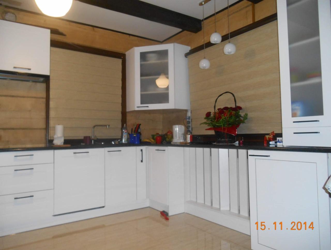 Jasna kuchnia w Daleszycach z białymi frontami, czarnym blatem i drewnianymi elementami wykończeniowymi, oświetlona trzema kulistymi lampami wiszącymi nad blatem, z bukietem czerwonych róż...