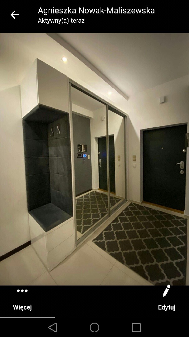 Nowoczesna szafa wnękowa z lustrzanymi drzwiami przesuwnymi i siedziskiem w przedpokoju w Daleszycach, widoczny dywan z geometrycznym wzorem.