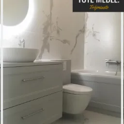 Jasnoszara szafka łazienkowa z dwiema szufladami, okrągłe lustro z podświetleniem LED, wisząca toaleta i fragment wanny na tle marmurowych płytek.