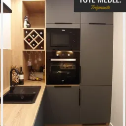 Nowoczesna kuchnia w odcieniach szarości z drewnianymi akcentami, zabudowa z piekarnikiem i mikrofalówką, czarny zlew i bateria, półki na wino i kieliszki, logo 'TOTE MEBLE. Trójmiasto' w prawym...