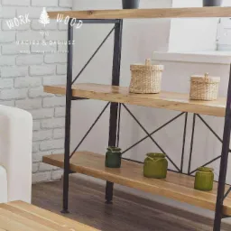 Regał z drewnianymi półkami na metalowym stelażu, prezentowany w jasnym wnętrzu w Poznaniu, z widocznymi dekoracyjnymi koszykami i zielonymi słoiczkami.