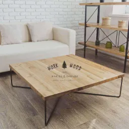 Kwadratowy stolik kawowy z jasnego drewna na metalowych nogach, z nadrukowanym logo 'Work Wood' w salonie z białą cegłą i sofą.