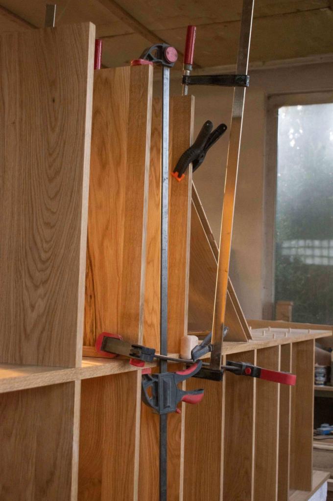 Fragment konstrukcji z drewna klejonego, prawdopodobnie szafy lub regału, podczas montażu z użyciem ścisków stolarskich i listwy. Widoczne połączenia na kołki.