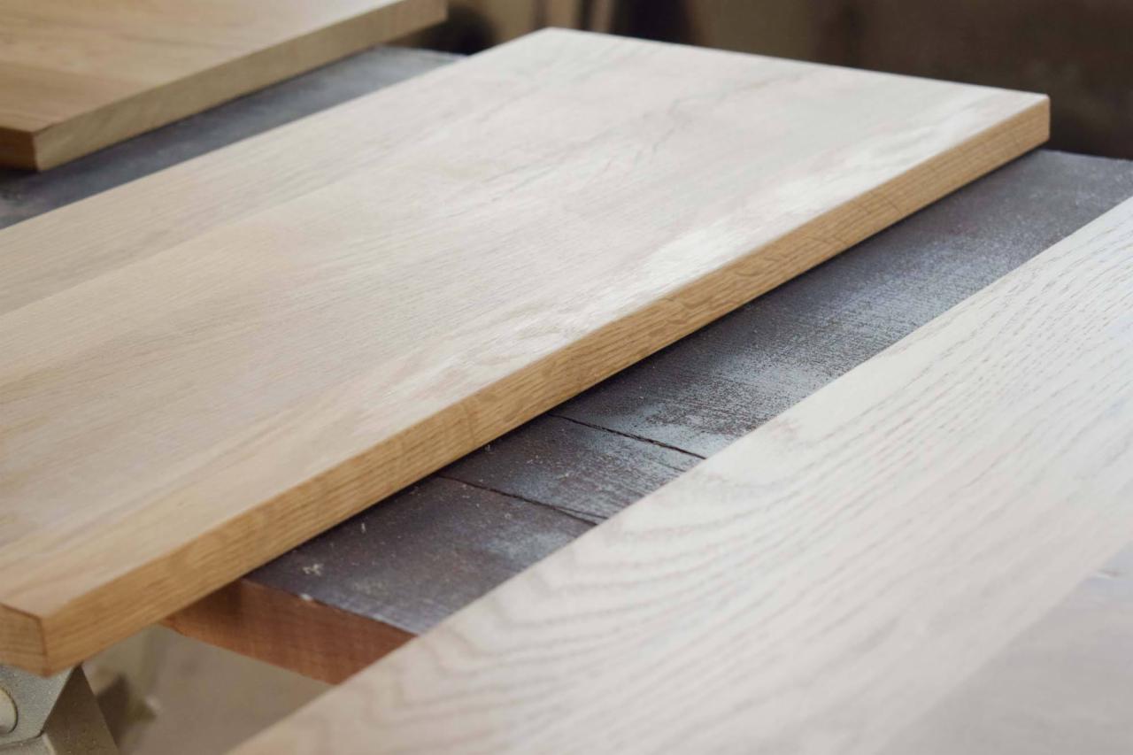 Surowe, jasne blaty drewniane w warsztacie, jeden z widocznym zaokrąglonym kantem, leżące na stole roboczym.