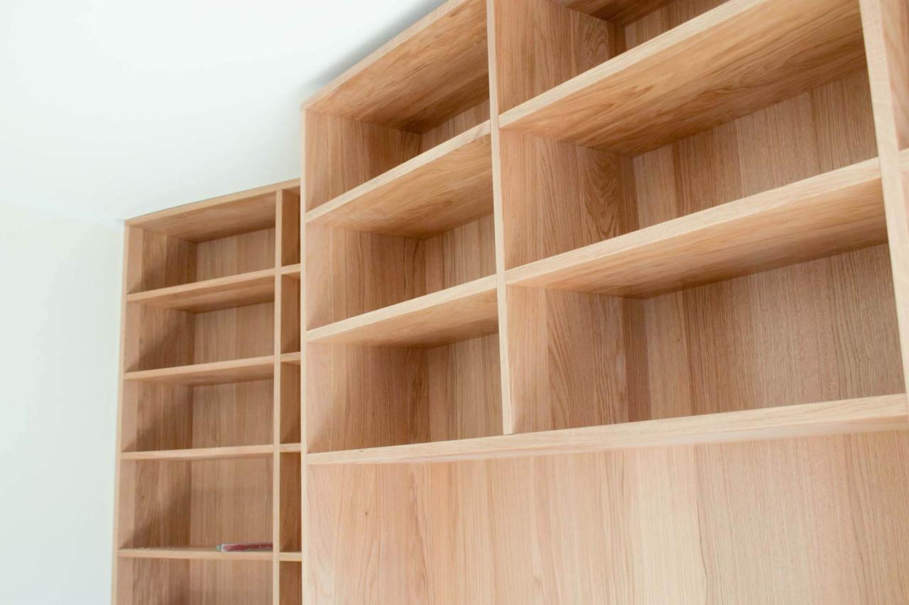 Dwie jasne, drewniane szafy wnękowe z półkami, wykonane z drewna o wyraźnym usłojeniu, ustawione pod kątem w jasnym pomieszczeniu.
