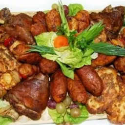 Udekorowany półmisek z pieczonym mięsem, kiełbasami, szaszłykami i owocami, całość na liściach sałaty.