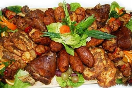 Udekorowany półmisek z pieczonym mięsem, kiełbasami, szaszłykami i owocami, całość na liściach sałaty.