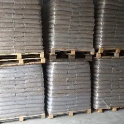 Magazyn worków z pelletem ułożonych w stosy na paletach, owiniętych folią stretch.