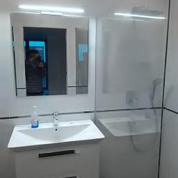 uslugi ogólno budowlane - Nowoczesna łazienka z białą szafką pod umywalką, lustrem z oświetleniem LED i przeszkloną kabiną prysznicową z chromowaną baterią.