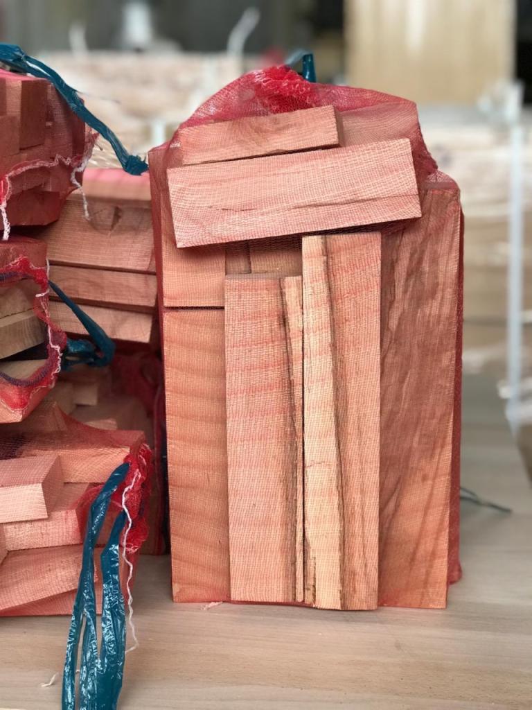 Worki z pociętym drewnem kominkowym w magazynie, widoczne struktury drewna i czerwone siatki worków.