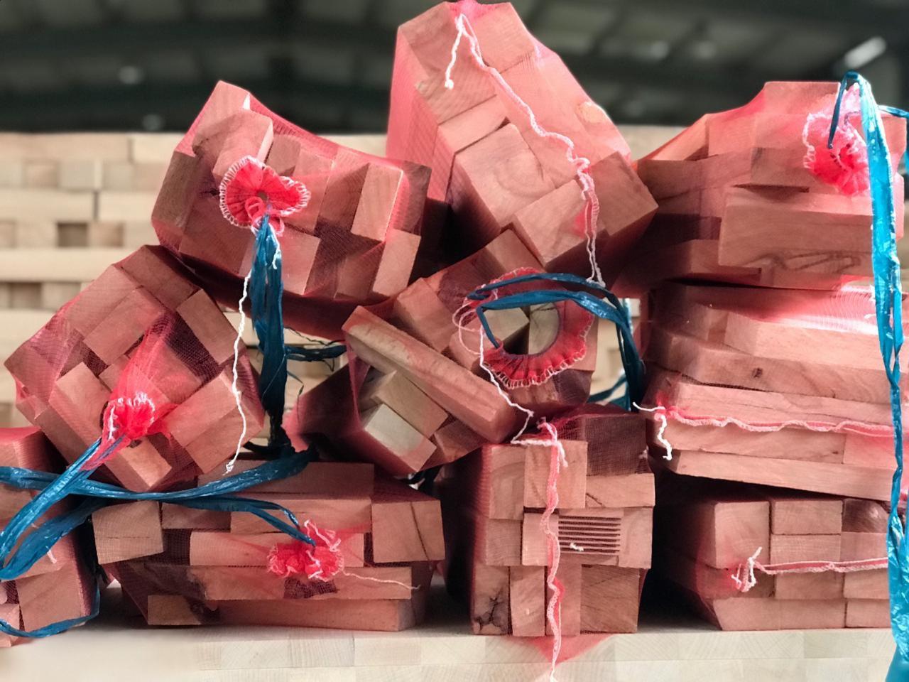 Stos pakowanych kawałków drewna kominkowego w czerwonych siatkach z niebieskimi uchwytami, ułożonych na jasnej powierzchni.