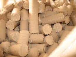 Stos cylindrycznych brykietów drzewnych o jasnej barwie, widoczne ślady po procesie prasowania, ułożone chaotycznie w dużej kupie.