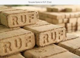 Ułożone kostki brykietu z widocznym wytłoczonym napisem 'RUF', lekko rozmyte tło z kolejnymi kostkami, ciepłe oświetlenie.