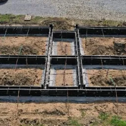 Przygotowanie szalunku pod fundamenty domu jednorodzinnego, widok z góry, częściowo zalany beton wewnątrz szalunku.