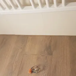 Podłączenie przewodów elektrycznych na drewnopodobnej podłodze przy białej ścianie z grzejnikiem.