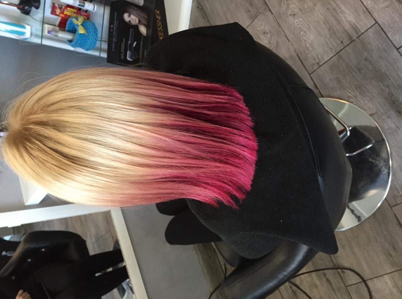 Blond włosy z różowymi końcówkami, widok z góry na fotelu fryzjerskim, w tle półka z kosmetykami.