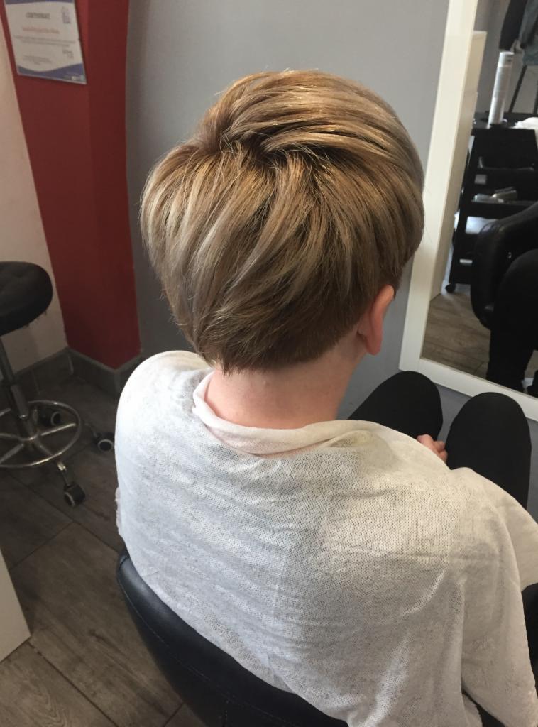 Krótkie, blond włosy z pasemkami, widok z tyłu, w salonie z czerwonym akcentem na ścianie.