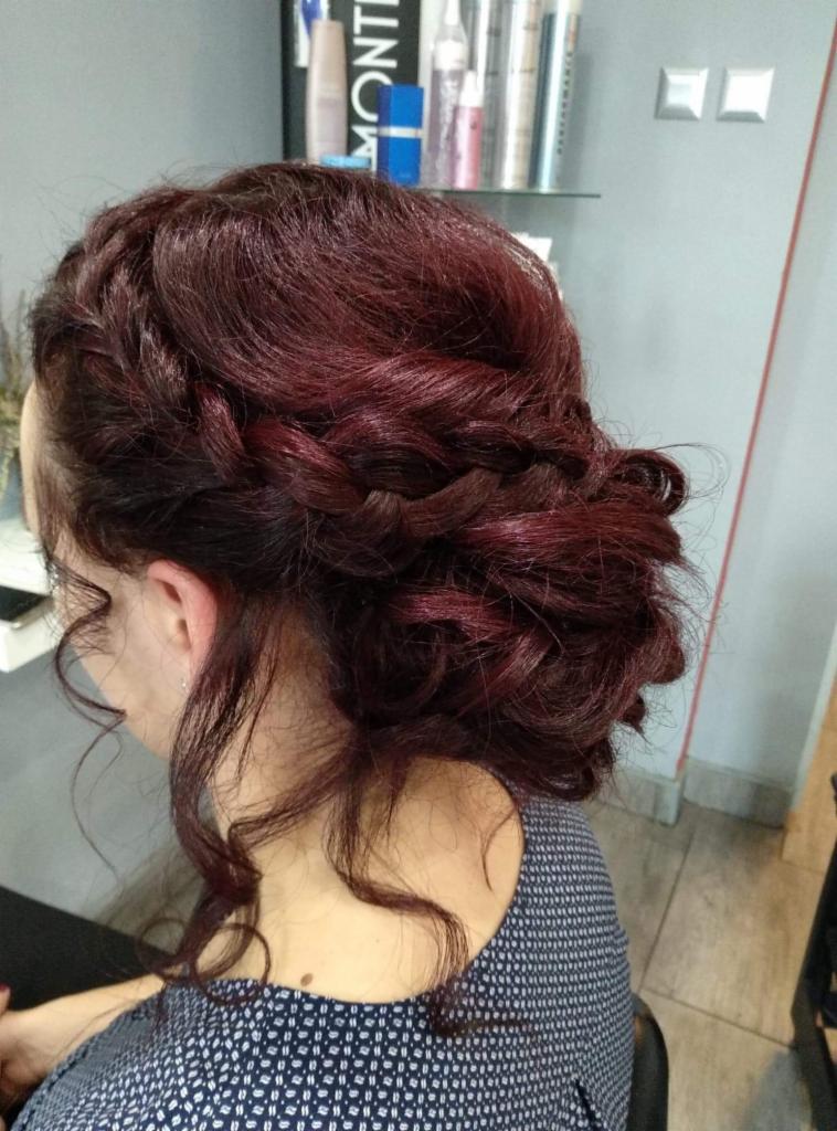 Upięcie z burgundowych włosów z warkoczem i luźnymi kosmykami, widok z boku, w tle półki z kosmetykami.