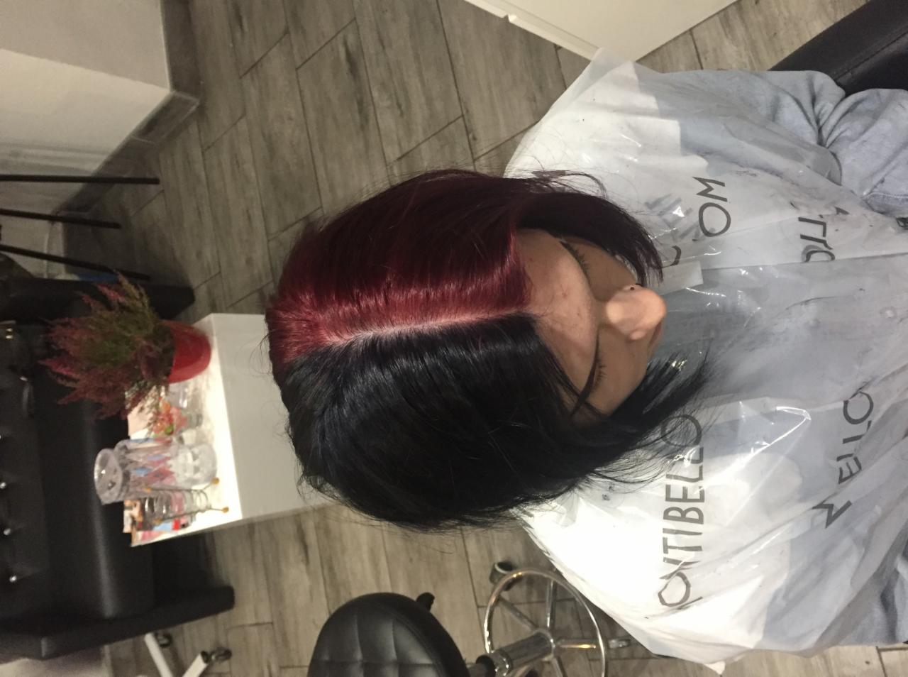 Widok z góry na kobietę w pelerynie ochronnej z włosami podzielonymi na dwie sekcje: czarną i bordową tuż po koloryzacji, siedzącą na fotelu.