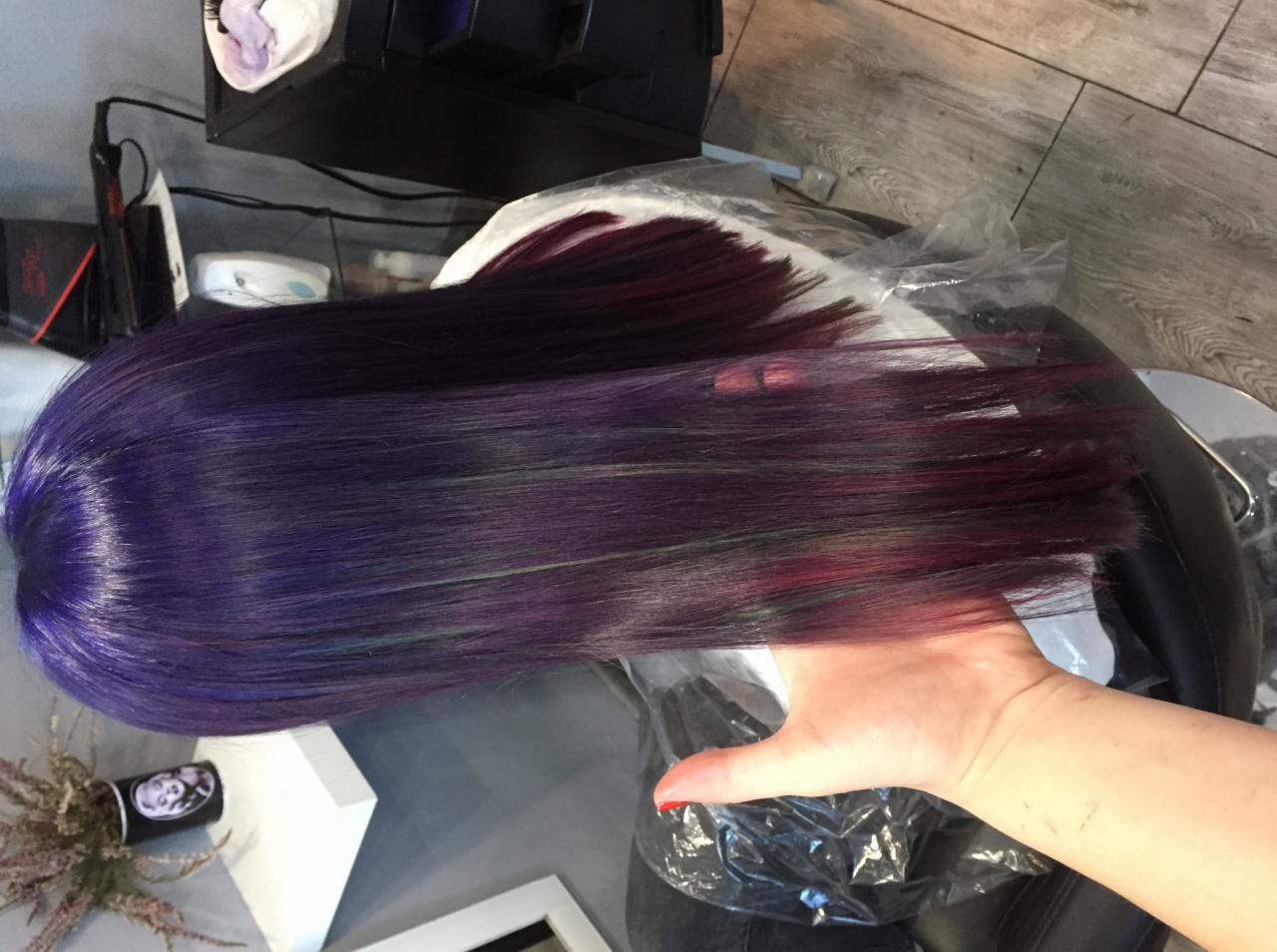 Świeżo ufarbowane, lśniące włosy w odcieniach fioletu i burgundu, trzymane w dłoni na tle fotela fryzjerskiego i podłogi.