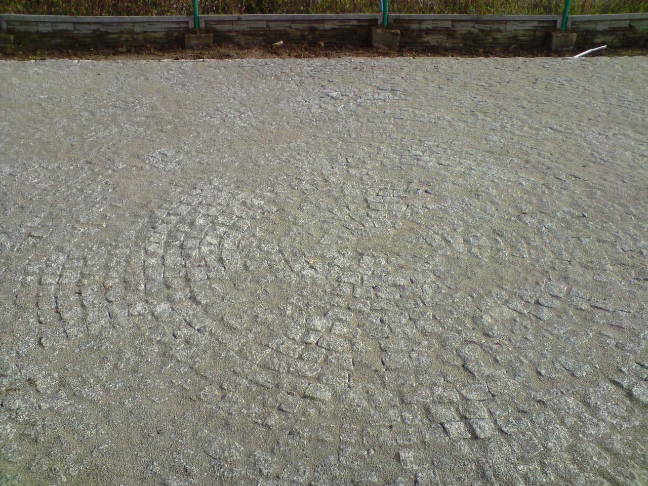 Ułożona nawierzchnia z szarej kostki w radialny wzór, widoczne zakończenie obrzeża.