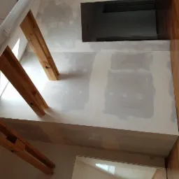 Sufit poddasza z drewnianą konstrukcją nośną, częściowo wykończony płytami gipsowo-kartonowymi i wstępnie zagruntowany, widok z dołu.