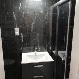 UsługiRemontowoBudowlane Tomasz Graczyk - Nowoczesna łazienka z czarnymi marmurowymi płytkami, białą umywalką z szarą szafką pod spodem oraz kabiną prysznicową z chromowanymi elementami.
