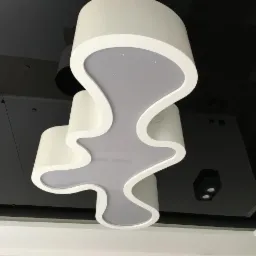 Nowoczesna, trójsegmentowa lampa sufitowa o organicznych kształtach, zamontowana na czarnym, błyszczącym suficie podwieszanym, z widocznymi punktowymi oprawami oświetleniowymi.